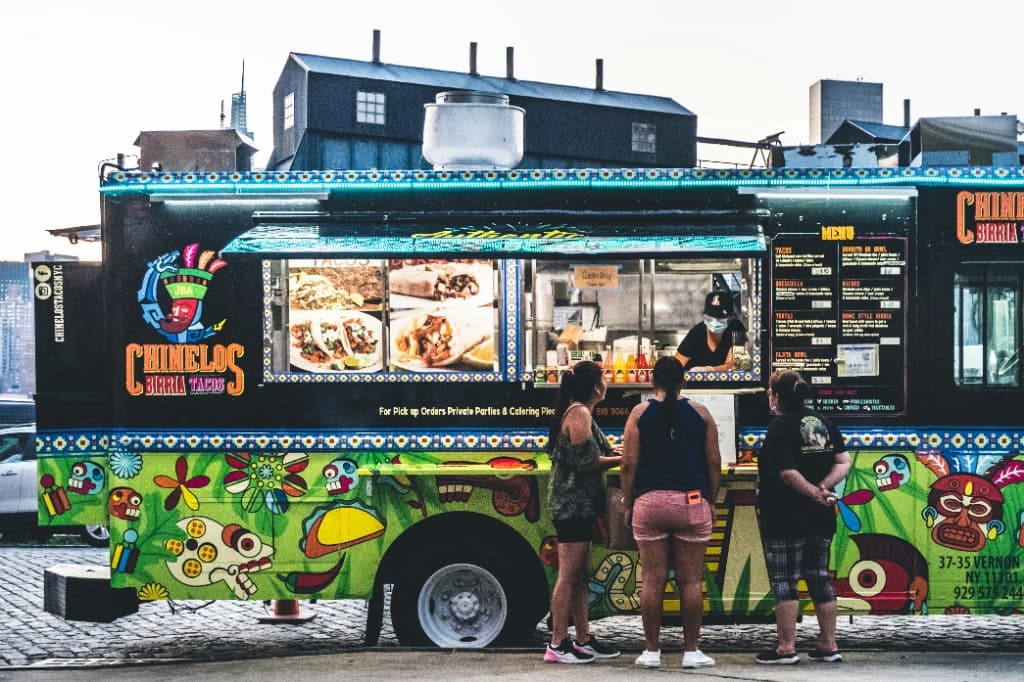 Colorful black food truck with customers lined up at the service window